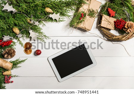 Juniper branches with a Christmas decor. Christmas, New Year background. Coniferous branches of juniper and white tablet with black screen. Top view, flat design.
