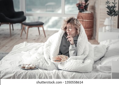 Junk Food. Blonde-haired Stressed Woman Eating Junk Food In Her Bed After Breakup With Boyfriend