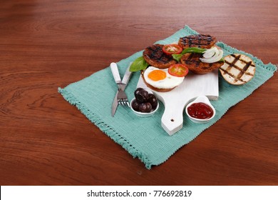 Junk Food Meat Big Beef Hamburger Fried Eggs On White  Wood Plate With Cutlery Ketchup Sauce And Pickels On Blue Mat Over Wooden Table