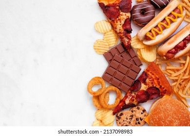 Junk Food Side Border Over A White Marble Background. Variety Of Take Out And Fast Foods. Pizza, Hamburgers, French Fries, Chips, Hot Dogs, Sweets. Above View With Copy Space.