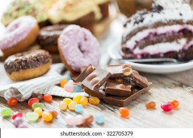 junk food, sweets and unhealthy eating concept - close up of chocolate pieces, jelly beans, glazed donuts and cake on wooden table