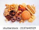 Junk food table scene. Collection scattered over a white marble background. Mixture of take out and fast foods. Pizza, hamburgers, french fries, chips, hot dogs, sweets. Overhead view.