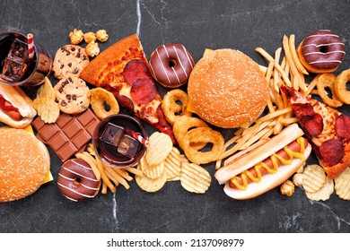 Junk Food Table Scene Scattered Over A Dark Background. Mixture Of Take Out And Fast Foods. Pizza, Hamburgers, French Fries, Chips, Hot Dogs, Sweets. Above View.