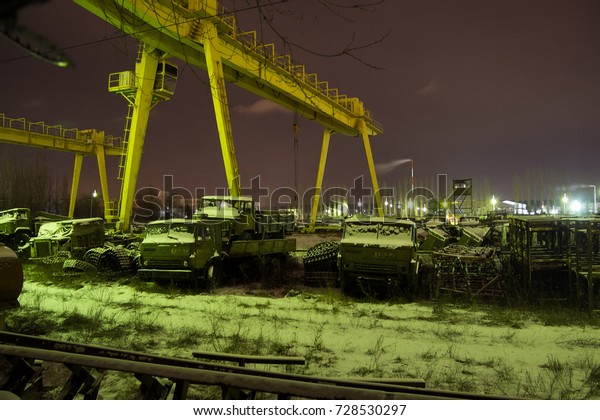 Junk yard of Russian military vehicle and tanks.\
Repair factory, crane at\
night