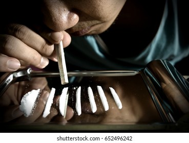 Junkie is snorting cocaine powder with rolled banknote. Narcotics concept.
