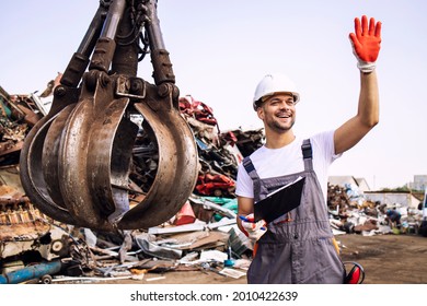 Junkyard worker waving to the crane operator to start lifting scrap metal parts.