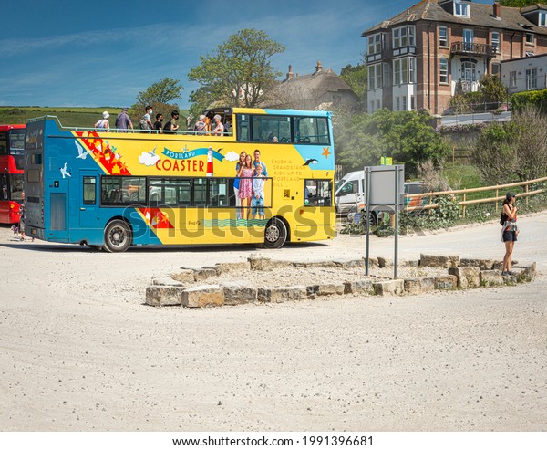 Jurassic Coaster\
open top bus with tourists embarking off in Lulworth Cove dusty car\
park with blue sky and a hot summer\'s day. West Lulworth, Wareham,\
Dorset. Taken 14th June 2021\
