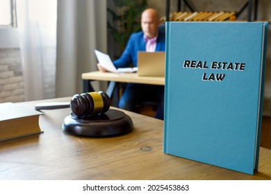 Jurist Holds REAL ESTATE LAW Book. Real Estate Law encompasses The Purchase And Sale Of Real Property, Meaning Land And Any Structures On It
