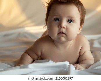 Just Beautiful. Cute Smiling Baby. Cute 3 Month Old Baby Girl Infant On A Bed On Her Belly With Head Up Looking With Her Big Eyes. Natural Bedroom Light. Infant Baby. Healthy And Medical Concept