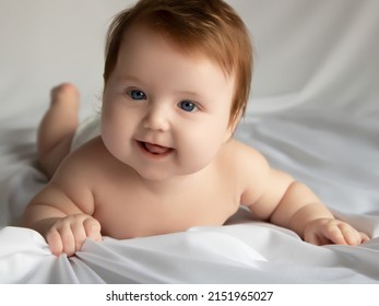 Just Beautiful. Cute Smiling Baby. Cute 3 Month Old Baby Girl Infant On A Bed On Her Belly With Head Up Looking With Her Big Eyes. Natural Bedroom Light. Infant Baby. Healthy And Medical Concept