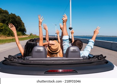 Just fun and road ahead. Rear view of young happy people enjoying road trip in their convertible and raising their arms up - Powered by Shutterstock