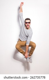  Just Having Fun. Excited Young Man Jumping In Front Of The White Wall And Keeping Mouth Open 