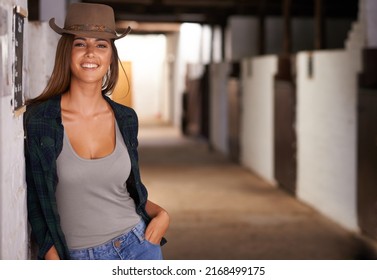 Just horsin around. A portrait of a beautiful young cowgirl leaning against a wall in a stable.