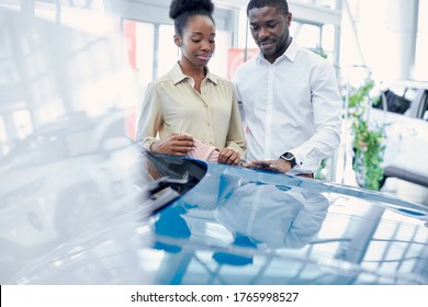 Just Imagine Us On The Road. Portrait Of Happy African American Couple Checking Out A Car In Modern Dealership, They Choose New Car Together