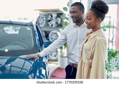 Just Imagine Us On The Road. Portrait Of Happy African American Couple Checking Out A Car In Modern Dealership, They Choose New Car Together