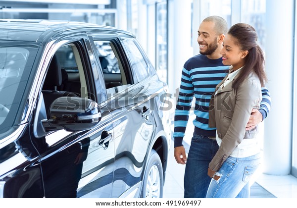 Just imagine us on the road. Shot\
of a happy African couple checking out a car at the\
dealership