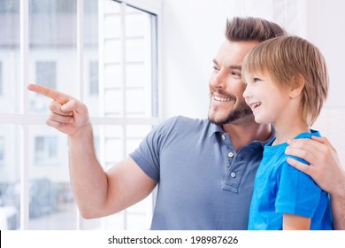 Just look over there! Happy father and son standing near the window while father pointing away and smiling