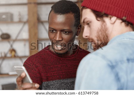 Just look at this! Stunned and shocked young black male in casual sweater using smart phone, showing his white friend watch of his dreams on internet that he now can buy at much cheaper price