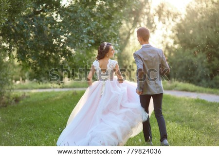 Just married loving hipster couple in wedding dress and suit on green field in a forest at sunset. happy bride and groom walking running and dancing in the summer meadow. Romantic Married young family
