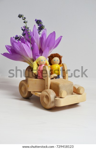 Just married toy couple in a wooden car with\
flowers on the white\
background
