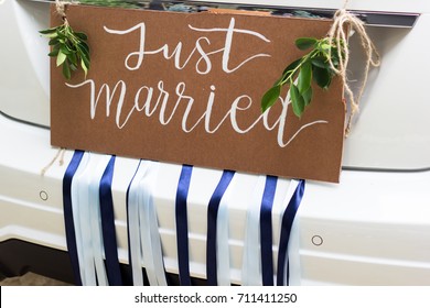 Just married vintage sign decorate with green leaves and blue ribbon on the modern car.