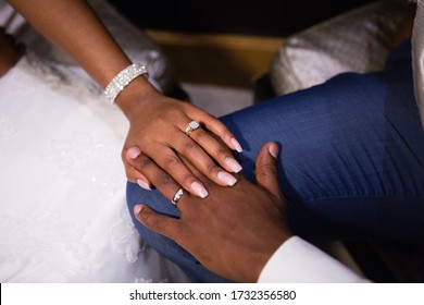 Just married young African couple's hands, holding together, new golden rings with diamonds, long fingers, wedding manicure, shiny wedding bracelet, white dress, blue groom's suit, white shirt