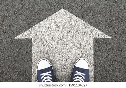 Just Move On, Keep Going. Blue sneakers on the asphalt road with drawn arrow. Top view,