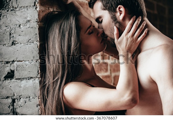 1回だけキス れんがの壁の近くに立ってキスをする美しい若い恋人夫婦の側面 の写真素材 今すぐ編集