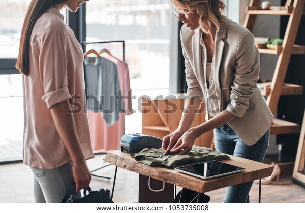 Just one moment. Beautiful young woman folding a shirt\
for her customer while working in the fashion boutique             \
  