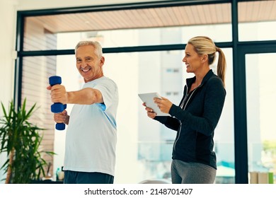 Just One More Rep To Go. Shot Of A Happy Physiotherapist Tracking Her Senior Patients Progress On A Tablet While He Lifts Weights.