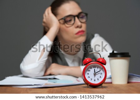 Just in time concept. Portrait of tired office worker wearing glasses and formal attire sitting at the table with papers and red alarm clock