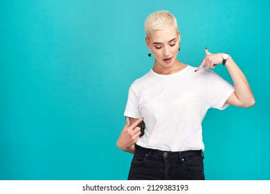 Just waiting for your words.... Studio shot of a confident young woman pointing at her t shirt against a turquoise background.