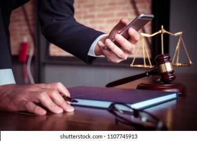 Justice and law concept. Gavel on sounding block in hand's Male judge at a courtroom, working with smart phone, report the case on table in modern office.