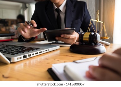 Justice And Law Concept. Male Judge In A Courtroom The Gavel,working With Digital Tablet Computer On Wood Table.