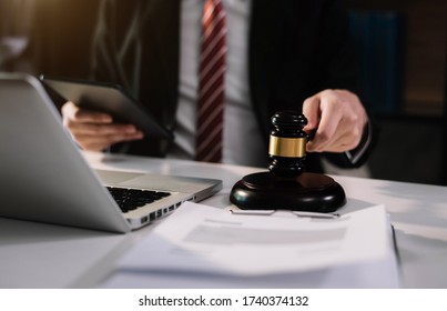 Justice And Law Concept.Male Judge In A Courtroom The Gavel, Working With Digital Tablet Computer On Wood Table In Sun Light.