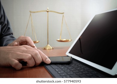 Justice And Law Concept.Male Lawyer In Office With The Gavel,working With Smart Phone And Digital Tablet Computer And Brass Scale On Wood Table