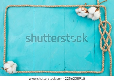 Jute rope rectangular frame, with a knot and cotton flowers, on blue painted boards, navy backdrop 