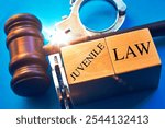 "Juvenile law" word with gavel and handcuffs on a blue background.