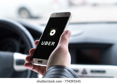 JYVASKYLA, FINLAND - DECEMBER 7, 2017: Man holding smartphone with Uber logo on screen in car. Uber is an American company offering transportation services online. Illustrative editorial.