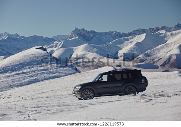 Kabardino-Balkaria, Russia - Oktober 2017:  Gray SUV
on the background of the landscape of pure white snow, blue sky and
winter mountains on a bright sunny day. Travel by car off road.
Side view
