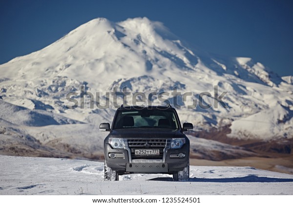 Kabardino-Balkaria, Russia - Oktober 2017:  Gray SUV\
Mitsubishi Pajero on the background of pure white snow, blue sky\
and winter Elbrus in the Caucasus Mountains, on a  sunny day.\
Travel by car off\
ro