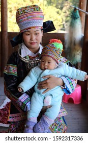 Kaili, China - October 29, 2019: At Hundreds of Birds Miao Village, portrait of a girl with her baby, wearing typical clothes and headgear of Miao minority