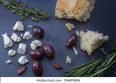 Kalamata Olives And Feta Cheese From Greece With Bread And Herbs Spread Out On A Dark Background Of Slate