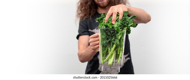 Kale smoothie food prep for a healthy green vegan and plant-based meal. Man adds green leafy greens to a blender jar which is full with green leaves.