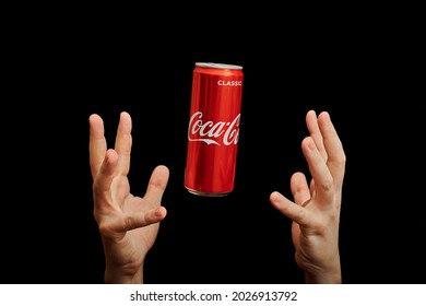 KALININGRAD, RUSSIA - MARCH 13, 2021 - Hands Catch Coca Cola Can, Black Background. Classic Coke Jar, Carbonated Soft Drink. Manufactured By The Coca-Cola Company.