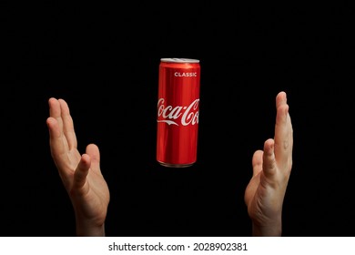 KALININGRAD, RUSSIA - MARCH 13, 2021 - Hands catch Coca Cola can, black background. Classic coke jar, carbonated soft drink. Manufactured by The Coca-Cola Company.