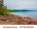 Kama Bay Beach in Nipigon Ontario Canada featuring colorful red and orange rocky shores, lake superior coastal line, overcast sky on summer day