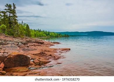 Kama Bay Beach in Nipigon Ontario Canada featuring colorful red and orange rocky shores, lake superior coastal line, overcast sky on summer day - Shutterstock ID 1976318270