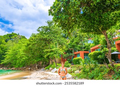 Kamala beach,Phuket,Thailand-May 11th 2024:Mature caucasian woman enjoying her vacation and Beautiful view of Kamala beach with lush beachside greenery against cloudy skies - Powered by Shutterstock