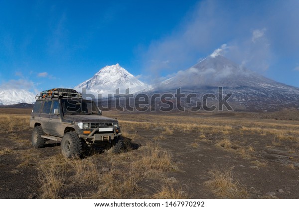 Kamchatka\
Peninsula - October 2, 2016: Toyota Land Cruiser Prado successfully\
delivers tourists along difficult routes, in the background\
Kluchevskaya group of volcanoes,\
Kamchatka.